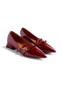 Ein Paar glänzende weinrote spitz zulaufende Schuhe mit niedrigem Absatz und doppelten Schnallengurten auf einem weißen Hintergrund.