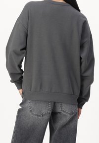Sudadera gris con un corte relajado, mangas anchas, dobladillo y puños acanalados. Combinada con unos jeans grises de tiro alto y desgastados que tienen bolsillos traseros.