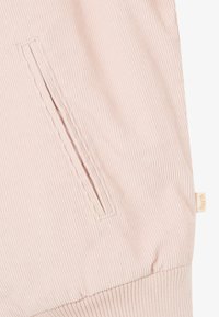 Lyserøde ribbet stof joggers med lomme i siden og elastisk talje, prydet med et lille mærke på siden med brandnavnet.