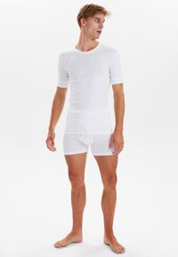 Hvid, tætsiddende skjorte med korte ærmer og boxershorts, lavet af et blødt, let stof med en glat overflade, minimale sømme og uden mønstre.
