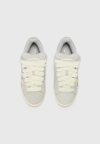 Gray suede sneakers with thick cream laces, rounded toe, cushioned collar, and subtle branding on the tongue and sides. Light-colored rubber sole.