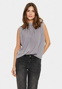 Blusa senza maniche grigia chiara con un collo alto e dettagli arricciati. Abbinata a jeans di jeans scuri con un design a cinque tasche.