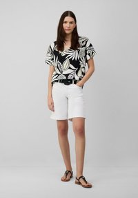 Schwarzes und weißes kurzärmliges Oberteil mit Blattmuster, kombiniert mit weißen, hochgekrempelten Shorts und schwarzen Sandalen. Strukturierter Stoff und lässige Passform.