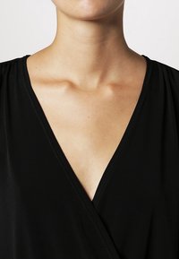 Vestido negro ajustado que presenta un escote en V con una tela suave, un ligero brillo y costuras sutiles a lo largo de los bordes.