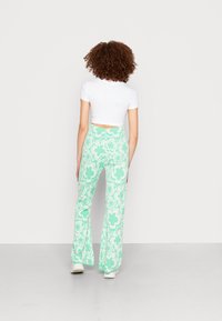 Calças fLared verdes menta com padrão floral, combinadas com uma blusa justa de manga curta branca. Ténis brancos simples completam o visual.