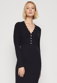 Langärmliges, marineblaues, geripptes Kleid mit tiefem V-Ausschnitt und einer Reihe dekorativer Knöpfe auf der Vorderseite. Glatte Textur und taillierte Silhouette.
