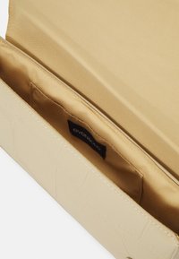 Beige käsilaukku, jossa on teksturoitu krokotiilikuosi, sisältä sileä satiinivuori ja pieni musta etiketti sisällä.