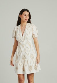 Vestito mini bianco con motivi a diamante e dettagli in pizzo, maniche a sbuffo corte, scollatura a V e gonna a strati.