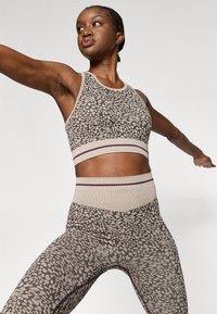 Aktiivne spordiriiete komplekt, mis sisaldab mustriga spordirinnahoidjat ja kõrge taljega legginsid beeži ja pruuni tooni. Omab kontrastset ääristust ja tekstureeritud kangaid.