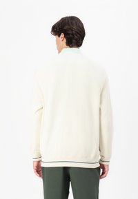 Maglione in maglia beige con accenti a strisce verdi e bianche al collo e ai polsini. Presenta una vestibilità rilassata e un tessuto testurizzato.