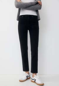 Černé džíny z denimu se slim fit střihem, středním pasem a minimalistickým designem. V kombinaci s bílými teniskami s černými akcenty.