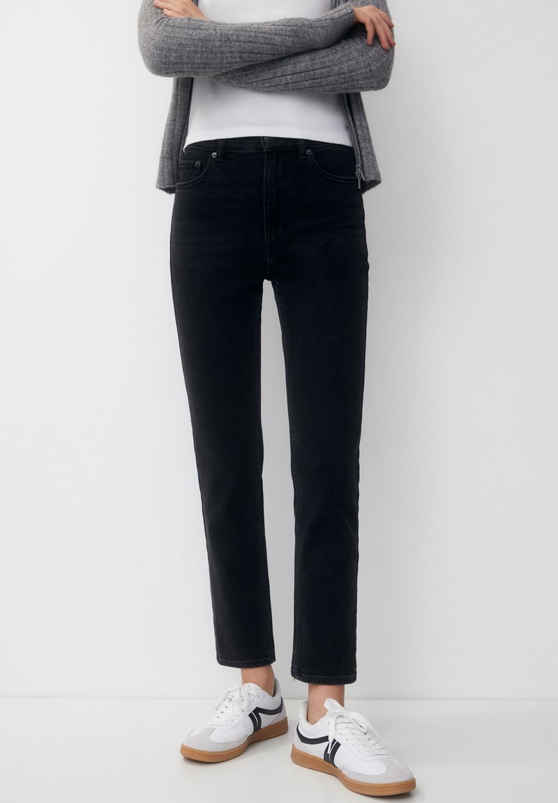 Černé džíny z denimu se slim fit střihem, středním pasem a minimalistickým designem. V kombinaci s bílými teniskami s černými akcenty.