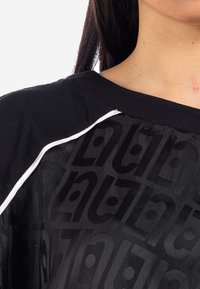 Top nero con un motivo monocolore texturizzato e un dettaglio in piping bianco lungo la spalla. Il materiale appare morbido e liscio.