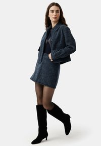 Conjunto de chaqueta y falda de tweed azul con un diseño estructurado, combinado con botas negras hasta la rodilla y medias transparentes. Textura suave.