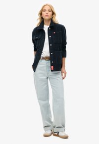 Marineblå cordjakke med fire forlommer, knaplukninger og en høj krave, parret med lyseblå højtaljede jeans og sneakers.