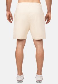Beige shorts met een elastische tailleband, zijzakken en een gladde textuur, gecombineerd met witte lage sneakers.