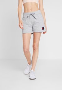 Grå bomullsshorts med elastisk midjeband, dragsko och logomärke. I kombination med vita sneakers på en neutral bakgrund.