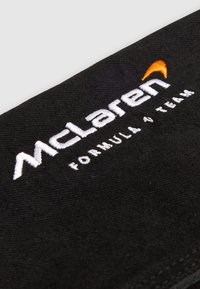 Black cotton fabric featuring embroidered white and orange "McLaren Formula 1 Team" text, with visible stitching texture.