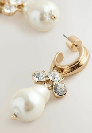 Guldtonade örhängen med en stor, pärlemorskimrande droppe och tre klara rhinstenar arrangerade i ett blommönster ovanför droppen.