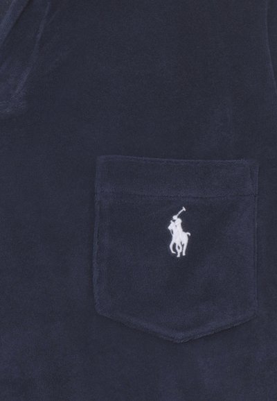 Tissu bleu marine avec une petite poche brodée d'un joueur de polo blanc à cheval tenant un maillet levé.