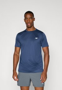 Marineblaues kurzärmliges Sporthemd mit strukturierter Oberfläche, ausgestattet mit einem kleinen weißen Logo auf der linken Brust, getragen mit grauen Shorts.