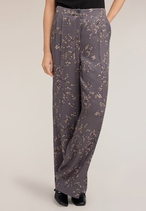 Kvinde iført grå bukser med høj talje og brede ben med et lille mønster af blomstergrene, parret med sorte spidse sko og en sort top.