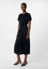 Granatowa sukienka do kolan z krótkimi rękawami i wiązanym przodem. Gładki, miękki materiał o luźnym kroju. W komplecie z czarnymi klapkami na obcasie.