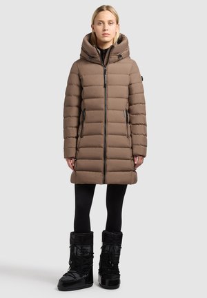 Brun polstret jakke med hætte, med lynlåslukning foran og sidelommer, parret med sorte isolerede støvler og leggings, på en neutral baggrund.