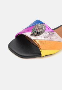 Sandalia de slip-on multicolor con tiras de cuero en púrpura, azul, plata, naranja y amarillo, con un adorno metálico decorativo.