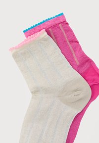 Δύο κάλτσες μέχρι τους αστραγάλους, μία ανοιχτό μπεζ με ροζ περίγραμμα και μία έντονο ροζ με μπλε περίγραμμα, και οι δύο με κάθετες υφασμάτινες ρίγες.