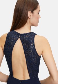 Navy Kleid mit komplizierter floralem Spitzenrücken, Ausschnitt-Design und Knopfverschluss, mit Paillettenakzenten entlang der Kanten.