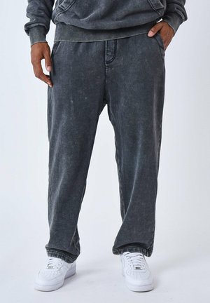 Joggers de algodón gris de corte relajado con un acabado desgastado, bolsillos laterales y puños elásticos, combinados con zapatillas blancas.