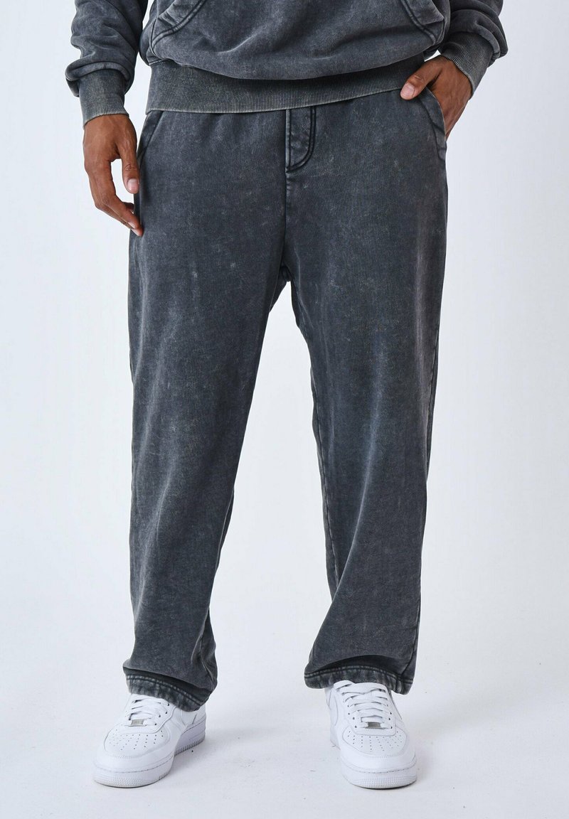 Joggers de algodón gris de corte relajado con un acabado desgastado, bolsillos laterales y puños elásticos, combinados con zapatillas blancas.