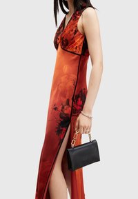 Maxikleid in einem Verlauf von Orange und Rot mit floralen Mustern, tiefem V-Ausschnitt, seitlichem Schlitz, kombiniert mit einer kleinen schwarzen Clutch.