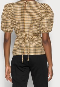 Blusa a quadri gialla e marrone, con maniche a sbuffo, vita con laccetto e chiusura a oblò sul retro. Realizzata in tessuto leggero.
