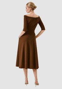 Abito marrone al ginocchio con maniche a 3/4, scollo a spalle scoperte, vita aderente e tasche, realizzato in tessuto liscio.