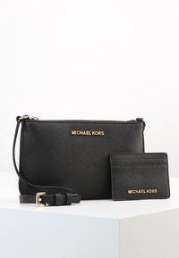 Borsa a tracolla in pelle nera con logo dorato, chiusura con zip, tracolla regolabile e un portacarte abbinato con lo stesso logo.