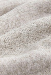 Lys beige tekstureret stof med blød, fuzzy overflade og let glans, der viser et bølge-lignende mønster og varieret tråd tæthed.