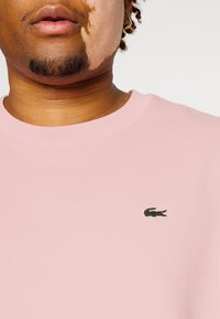 T-shirt a manica corta in cotone rosa con logo di coccodrillo verde ricamato sul petto. Texture liscia con vestibilità rilassata.