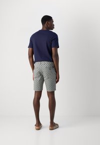 Marine t-shirt, gestreepte shorts met geometrisch ontwerp in beige en blauw, en beige sandalen. Model staat met de rug naar de camera.