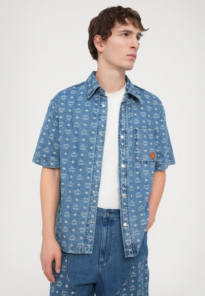 Denim short-sleeve shirt featuring a print of small repeated patterns, light blue color, and a chest pocket with orange accent.