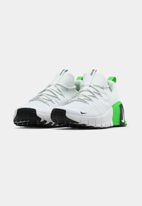 White athletic shoes with green accents, textured fabric upper, elastic laces, and a black rubber outsole featuring a prominent tread pattern.