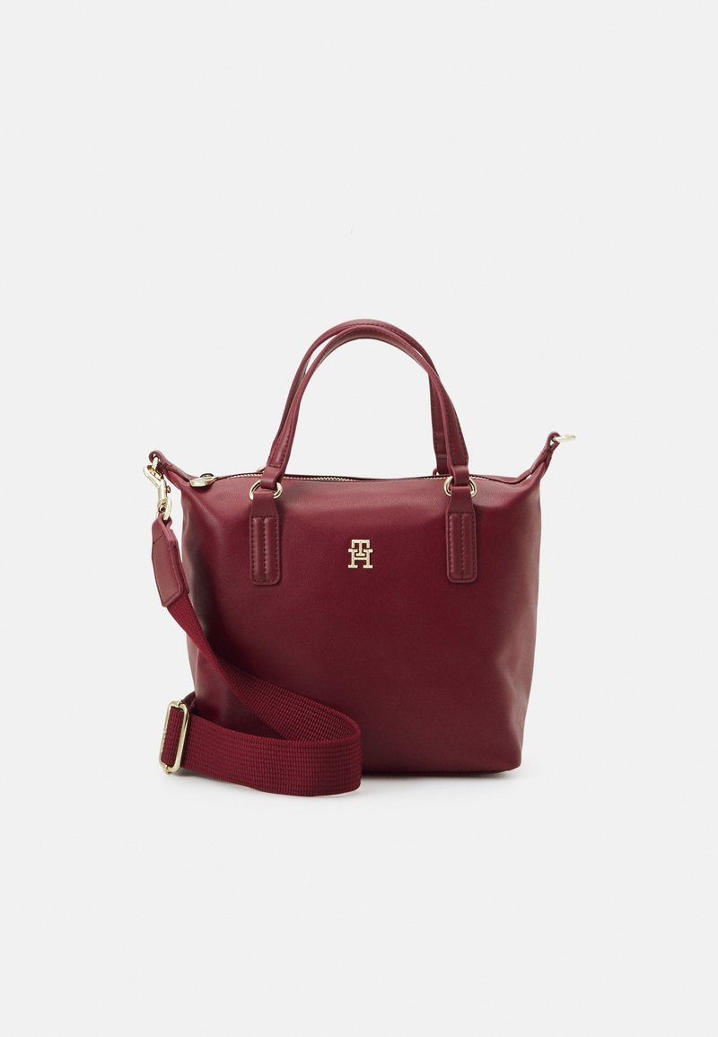 Sac à main en cuir bordeaux avec doubles poignées, bandoulière réglable et amovible, et emblème logo doré sur le devant.