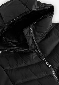 Sort puffers jakke med hætte, der har en glat overflade, quiltet design og en frontlynlås med brandet træk, der viser hvid skrift.