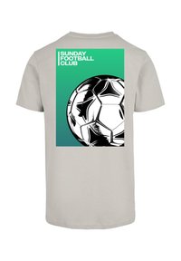 Svetlosivé tričko s čiernobielou grafikou futbalovej lopty a textom "NEDĚLNÝ FUTBALOVÝ KLUB" na pozadí so zeleným gradientom.