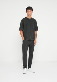 Tamno sivi oversized T-shirt kratkih rukava uparen sa uskim tamnim hlačama. Nosivo s bijelim tenisicama, protičnom uz jednostavnu bijelu pozadinu.