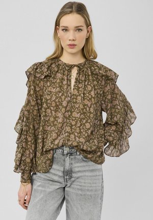 Blouse marron à motifs floraux avec manches à volants et détail découpé sur le devant. Confectionnée dans un tissu léger, elle présente une coupe ample et des motifs délicats en rose.
