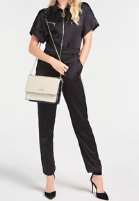 Mono de satén negro con mangas cortas y cierre de cremallera, combinado con un bolso en crema y negro con asa de cadena. Tacones de aguja negros.