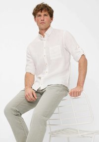 Witte linnen overhemd met knopen en een zak, gecombineerd met lichtgrijze jeans. Het overhemd heeft opgerolde mouwen en een losse pasvorm.