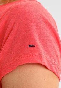 Koralli lyhythihainen t-paita, joka on valmistettu pehmeästä puuvillasta; siinä on pieni sininen, punainen ja valkoinen brodeerattu logo hihassa.